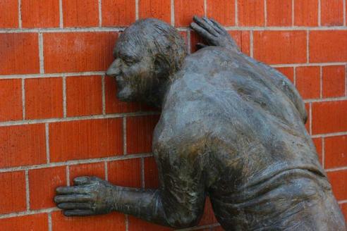 Mann aus Bronze hält Ohr an Backsteinwand